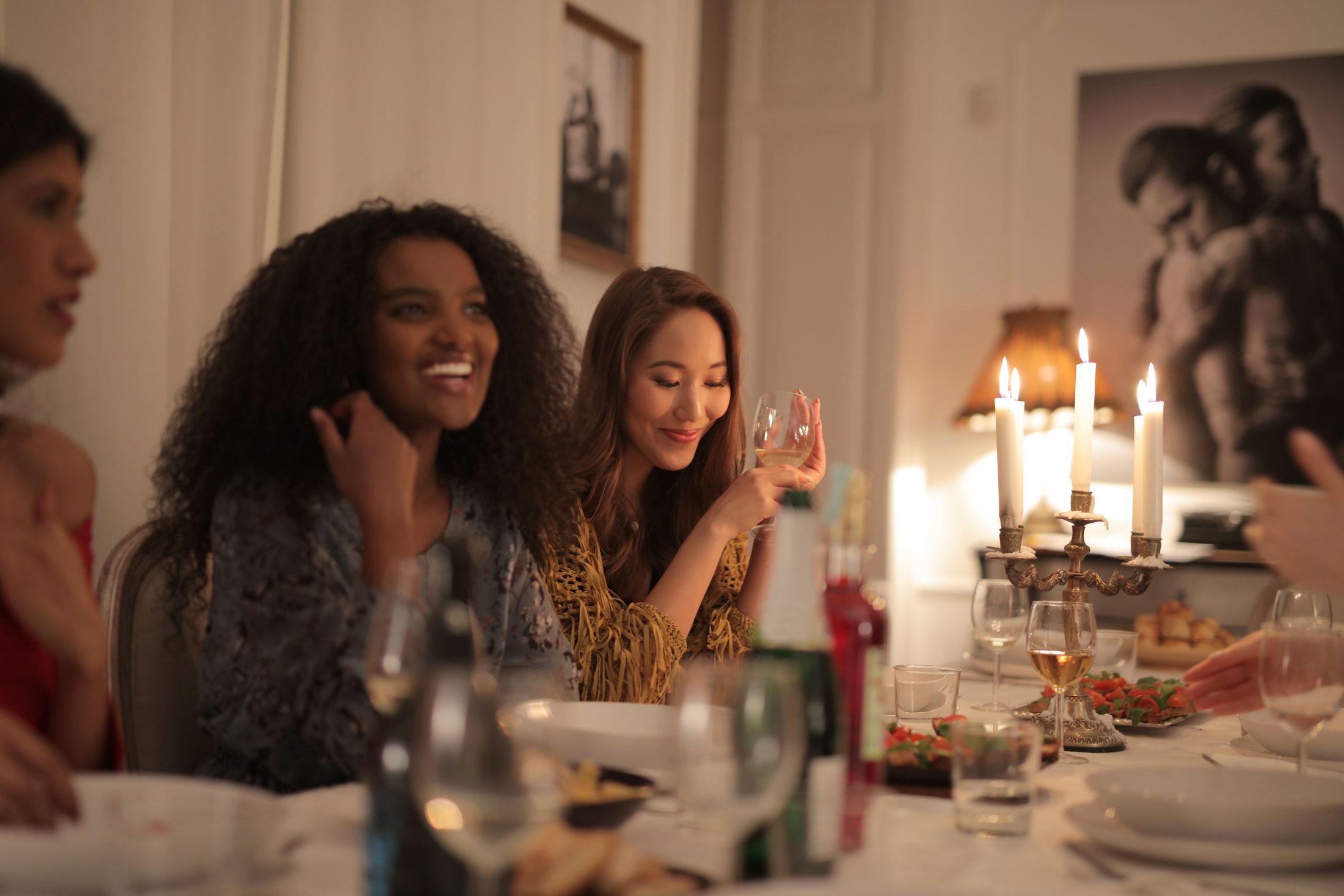 Women laughing together around a candlelit dinner table